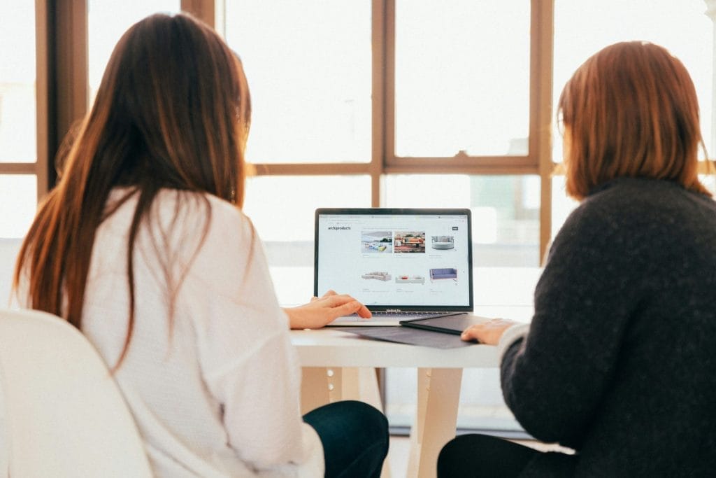 Two People Sat At Meeting Table Looking At Laptop